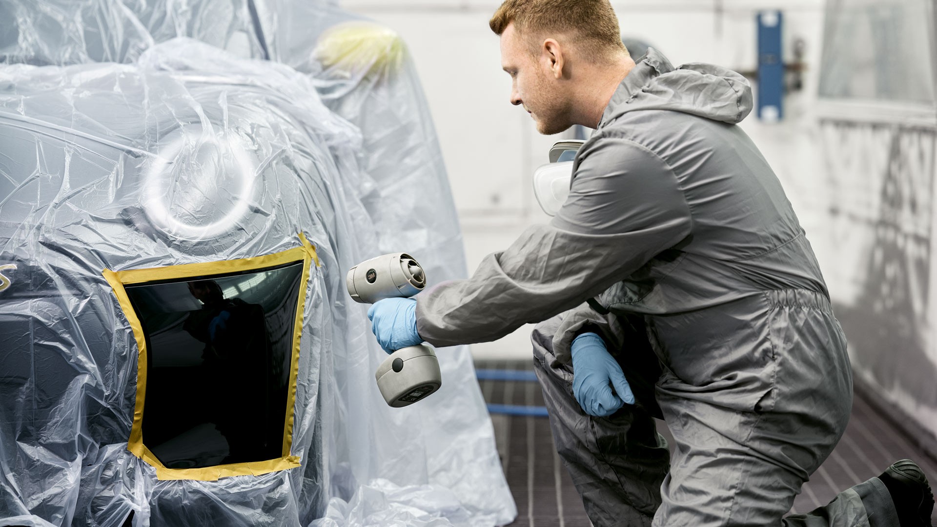 Technicien appliquant par pulvérisation une finition sur un panneau masqué d’une MINI.